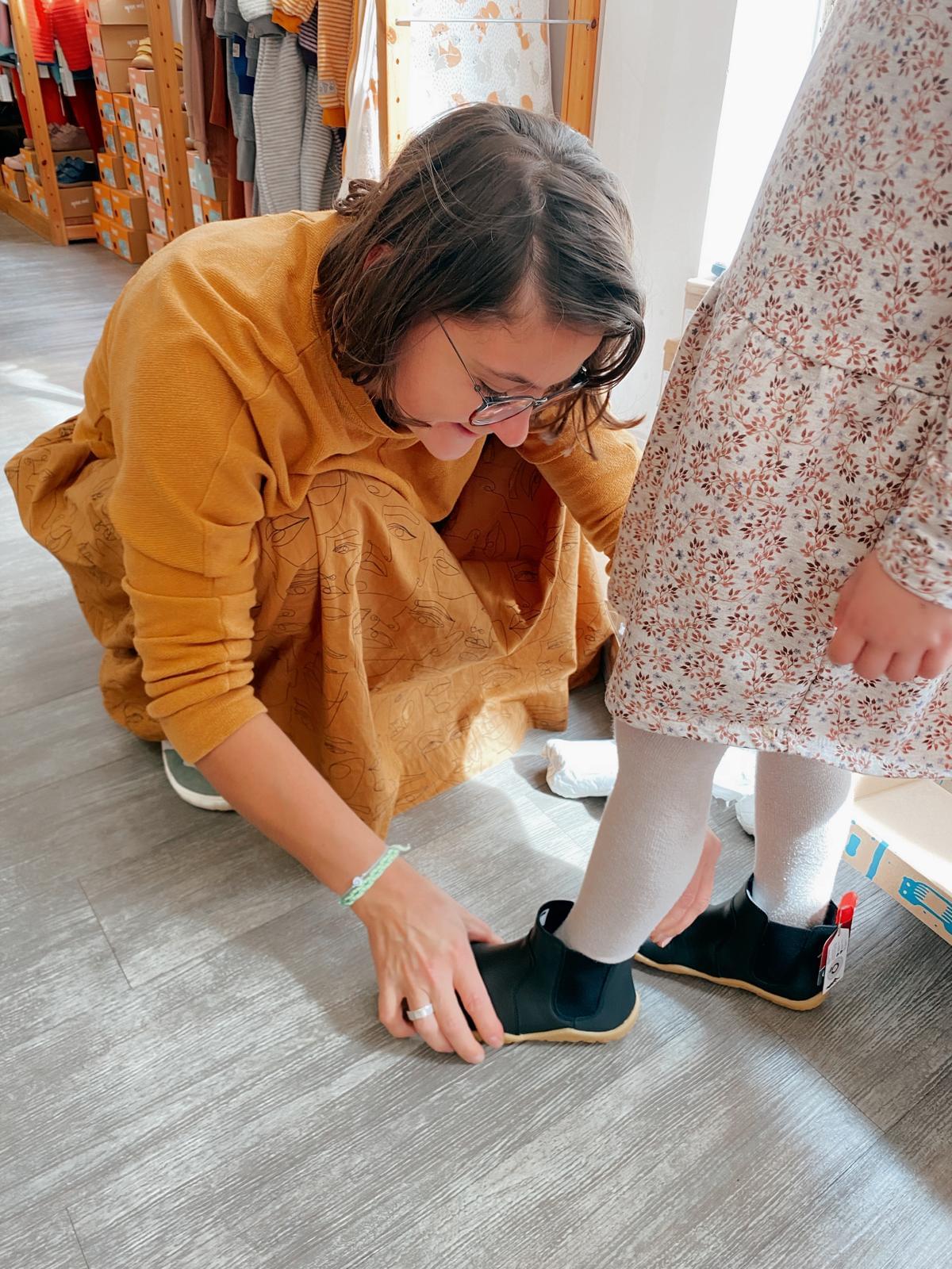 Frau passt einen Barfußschuh an Kindesfuß an.