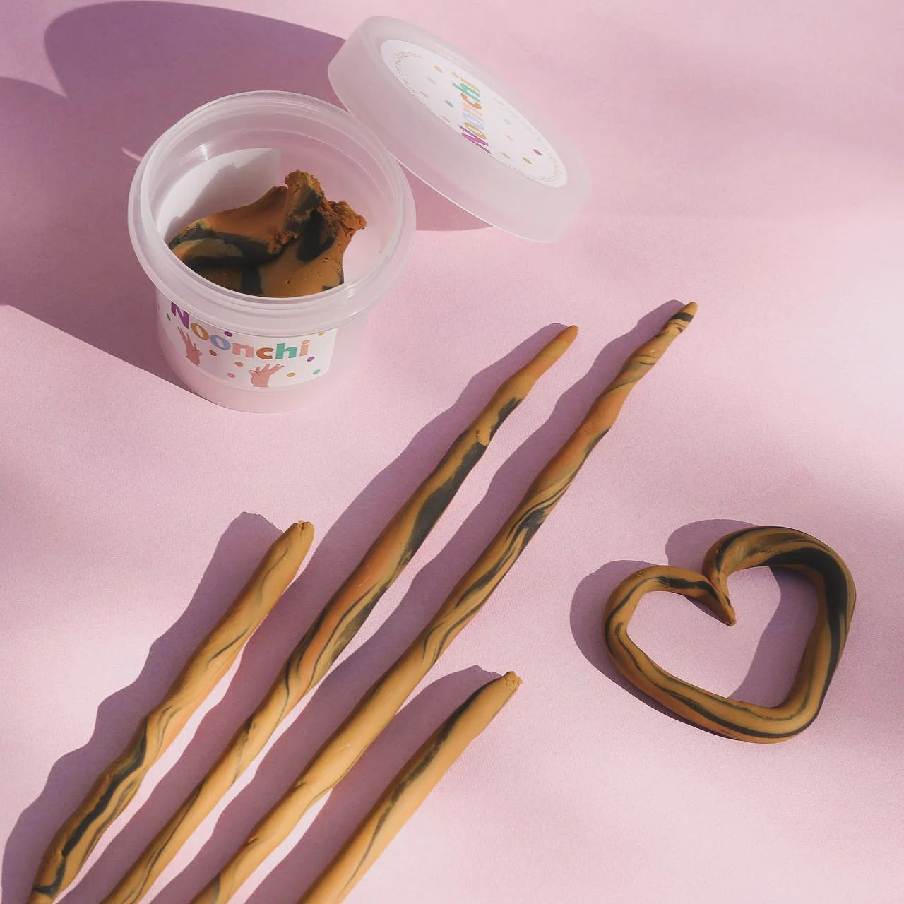 Noonchi Knete, Farbton Tiger, zur langen Streifen gerollt und ein geformtes Herz aus der Knete