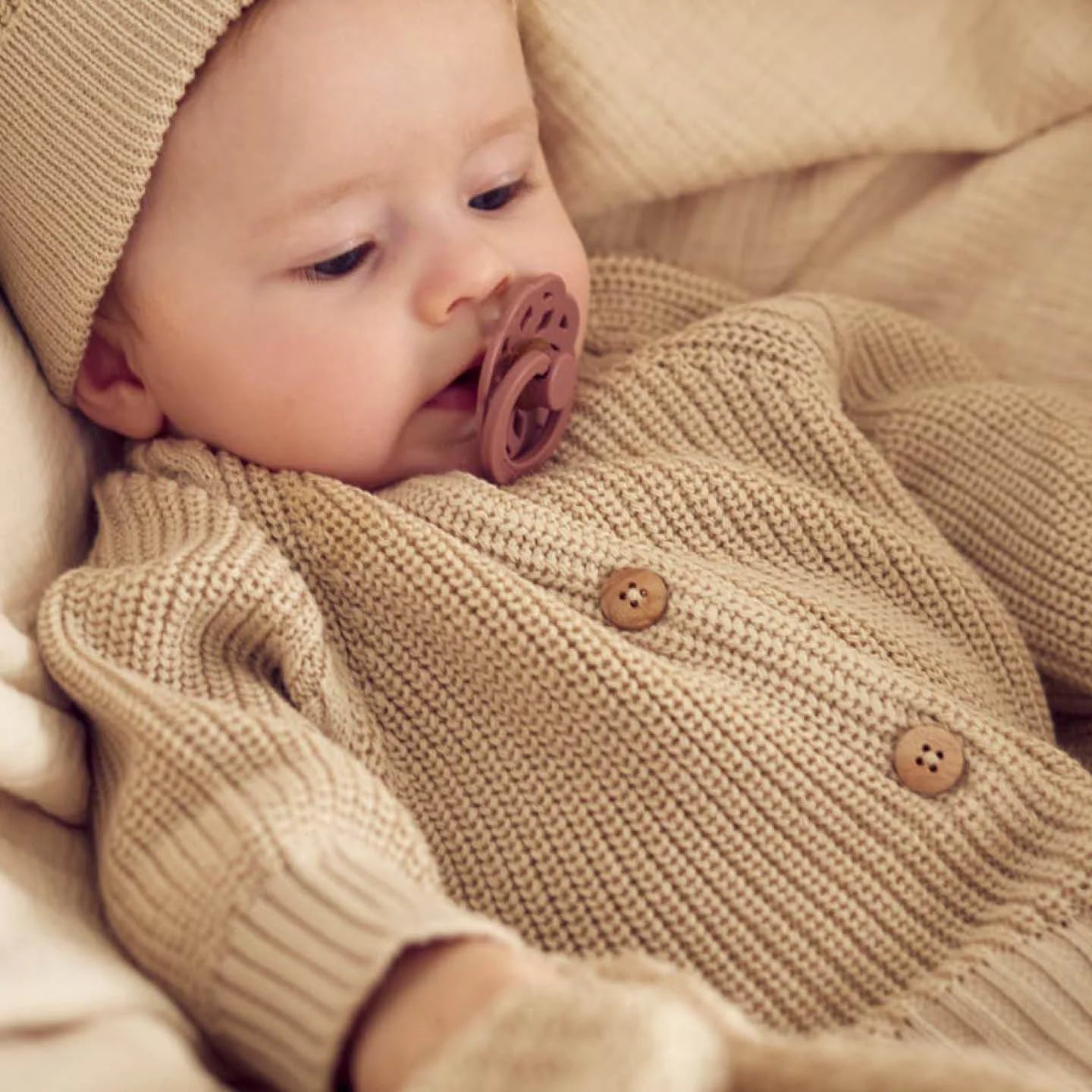 Baby trägt einen gestrickten Pullover aus Baumwolle, mit Schnuller im Mund